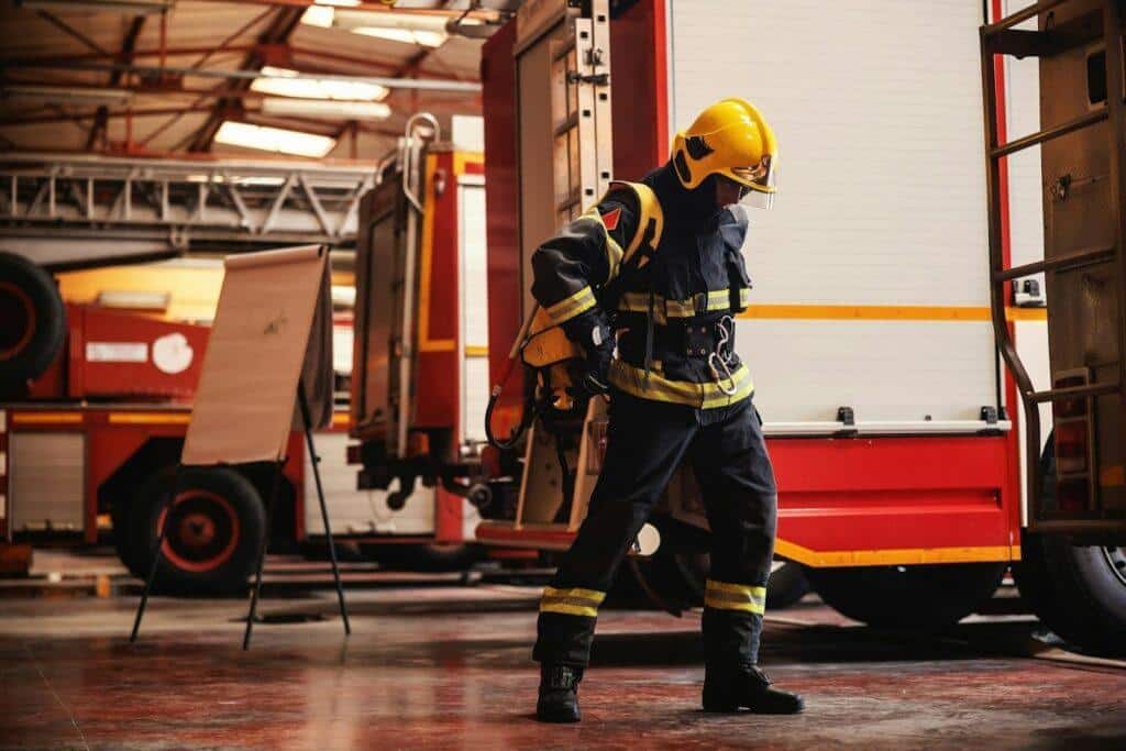A firefighter walks to their truck putting on their equipment and uniform