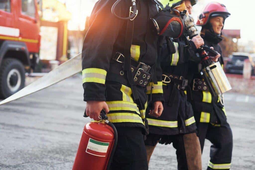 A group of firefighters walking into a building carrying equipment like fire extinguishers