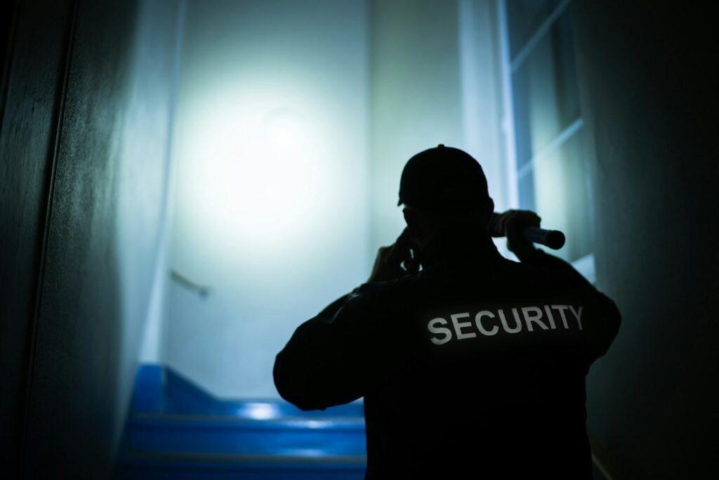 A security guard checks a hallway with a flashlight during a night shift