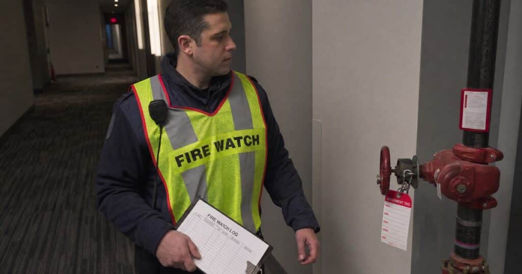 Fire watch guard in hi-vis vest checking a fire watch log during a patrol round
